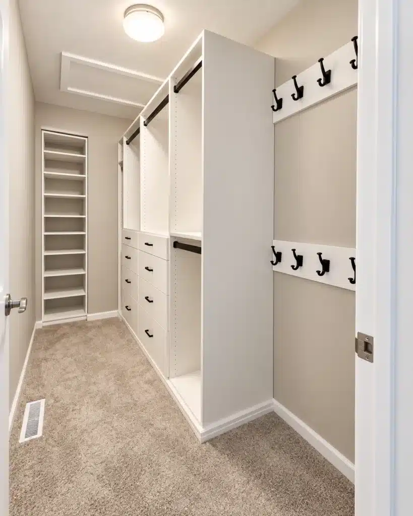 Custom walk-in closet organizer featuring white built-in drawers, adjustable shelving, hanging rods, and black hooks.